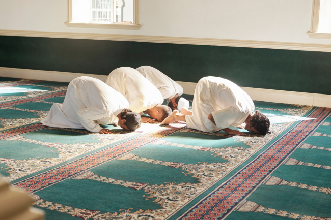 Muslim men in prostration (sujood) during prayer on a green mosque carpet, illustrating the two-rak'ah nafl prayer performed for Istikhara.