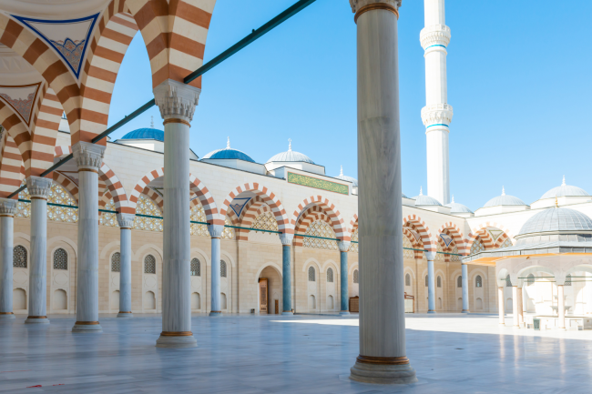 Grand mosque courtyard with marble columns and a minaret against a clear blue sky